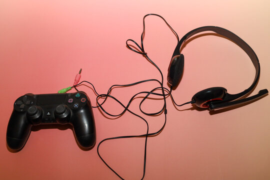 Lviv, Ukraine - March 19, 2026: A black wireless controller and a wired headset with a microphone are placed on a pleasant pink gradient background.