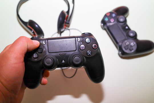 Lviv, Ukraine - March 19, 2026: ​A hand holds a black wireless console controller against a background of another gamepad and headphones.