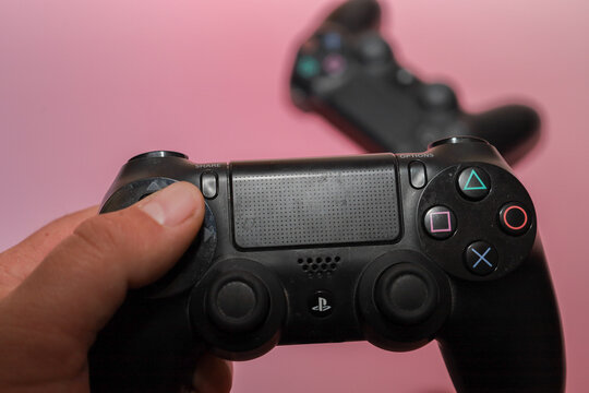 Lviv, Ukraine - March 19, 2026: A hand firmly holds a black gaming controller in the foreground, showcasing details of the buttons and touchpad.