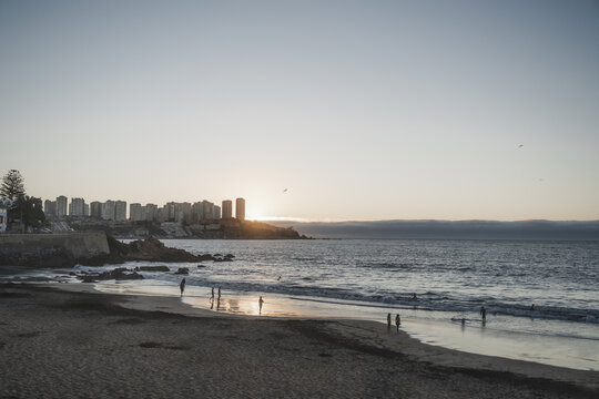 Atardecer en playa de Conc&oacute;n con siluetas de personas y edificios de fondo, Chile