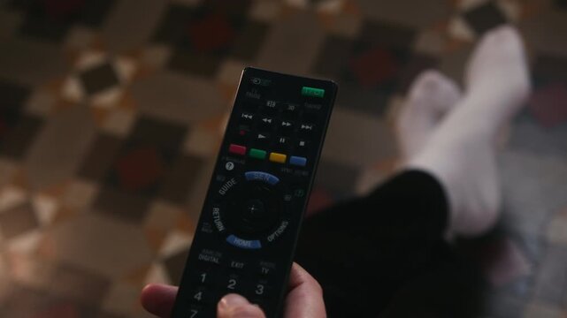 A young woman holding a TV remote, browsing channels in a cozy living room, enjoying a relaxed home atmosphere. High quality 4k footage