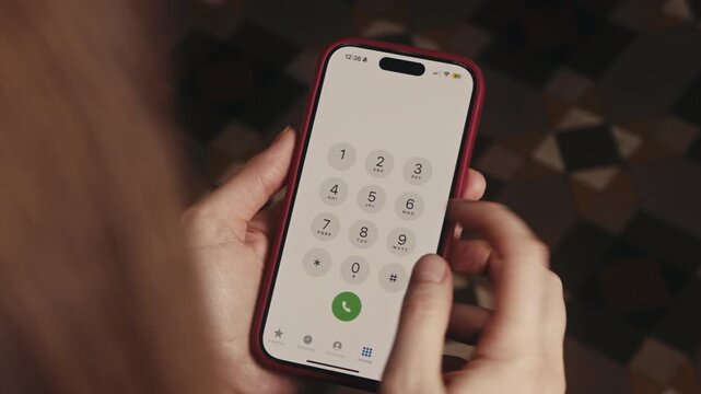 Over the shoulder view of a woman nervously dialing 911 on a smartphone. Her hands are shaking, showing stress and urgency in an emergency situation. High quality 4k footage