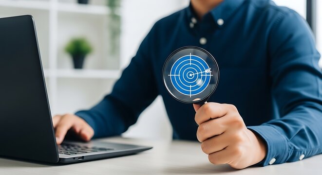 Businessman holding a magnifying glass with a blue radar target icon, searching for business opportunities on laptop