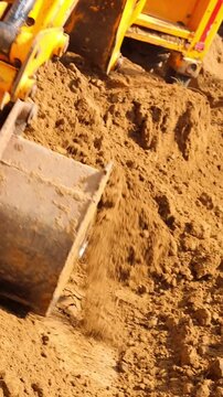 Heavy duty yellow JCB excavator bucket lifting and moving fresh brown soil to level the ground at a residential construction site or plot development project.
