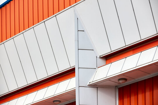 Architectural facade with orange white and blue cladding corrugated metal panels, glass windows of industrial or commercial building, contemporary architecture with vertical relief, material contrast.