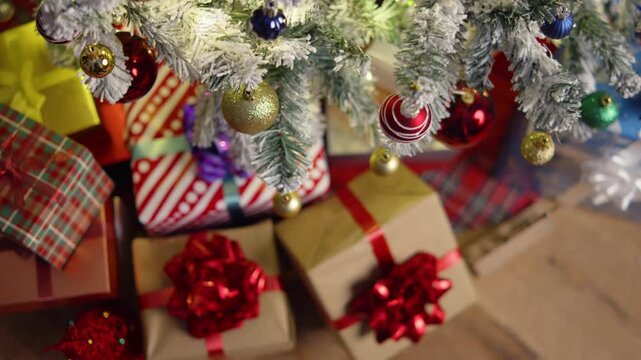 Cozy living room view: big stack of colorful Christmas gifts with shiny tapes and bows placed under the illuminated Christmas tree. Warm festive atmosphere, winter holidays concept.