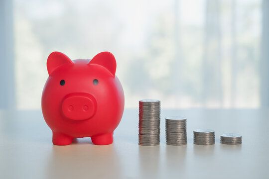 Red piggy bank with stacked coins showing decreasing levels, representing financial planning, savings strategy, expense management, and budgeting challenges in personal finance.