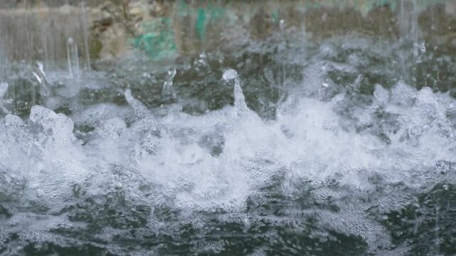 Water splashes violently across a dark green surface. Crisp droplets form in the frothy white water. Ripples spread through the disturbed surface. Fresh, energetic motion captures the moment