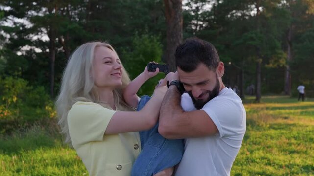 Sunset portrait with white parents holding toddler in meadow, mother adjusting hair, father supporting child, golden hour glow, candid embrace, soft laughter, casual clothing and natural