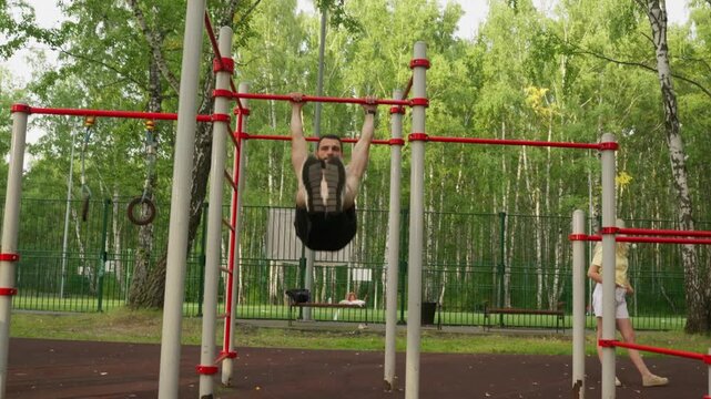 Shirtless male performing pullups on red bars, strict form and controlled tempo, core engaged, steady breathing, focused training session in birch park, onlookers in background, grit