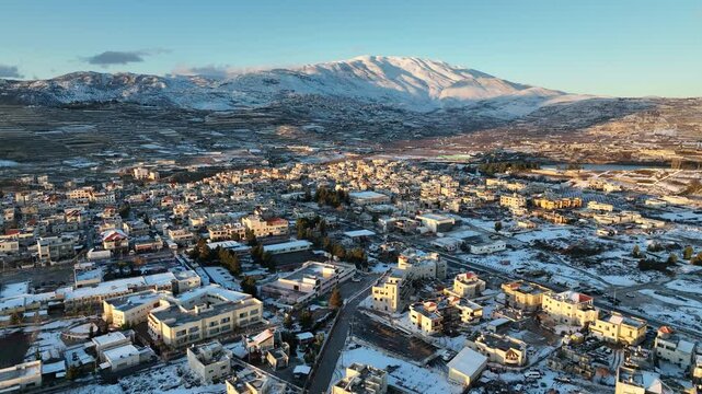 Aerial view of Mas'ade village and Odem Forest at sunset with snow-covered Mount Hermon, Golan Heights