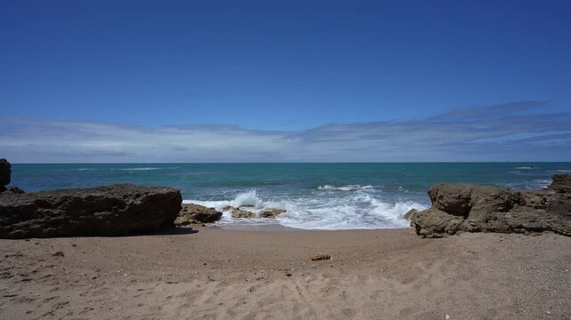 Small Secluded Rocky Beach in Chiclana de la Frontera Spain; Scenic Atlantic Ocean Waves Crashing on Sand at La Barrosa Coast in Andalusia with Blue Sky and Turquoise Water Establishing Shot