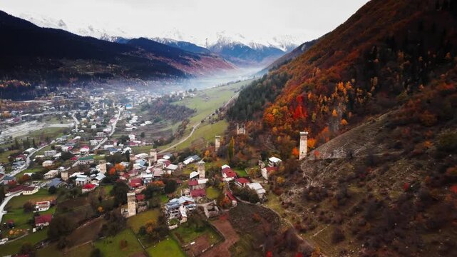 mountain village nestled in morning mist with church spire rising above tiled roofs, drone view captures patchwork fields and narrow lanes, cultural atmosphere and heritage architecture of Svaneti,