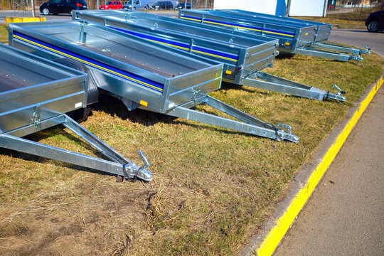 Row of new galvanized car utility trailers parked on grass for sale. Open metal cargo trailers for transportation, logistics and DIY projects.