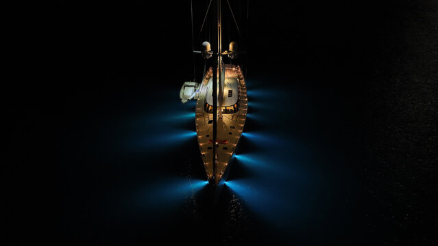 Aerial drone night shot of illuminated sail boat with wooden deck anchored in deep blue Aegan sea