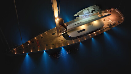 Aerial drone night shot of illuminated luxury yacht with wooden deck anchored in open ocean deep blue sea © aerial-drone