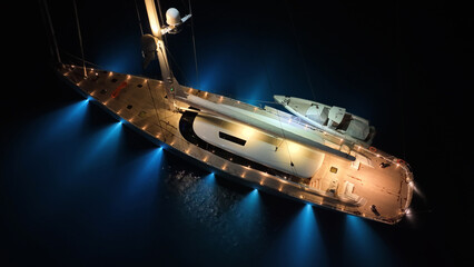 Aerial drone night shot of illuminated luxury yacht with wooden deck anchored in open ocean deep blue sea © aerial-drone