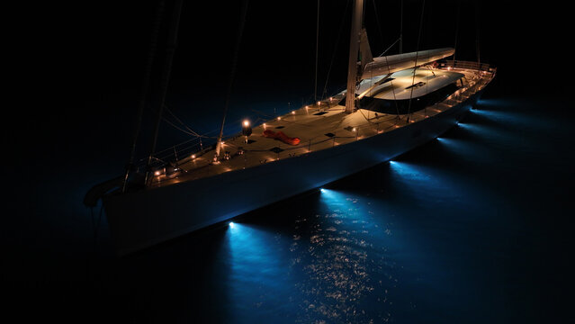 Aerial drone night shot of illuminated sail boat with wooden deck anchored in deep blue Aegan sea