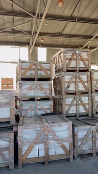 Rows of wooden crates filled with white building blocks are neatly stacked inside a large industrial warehouse