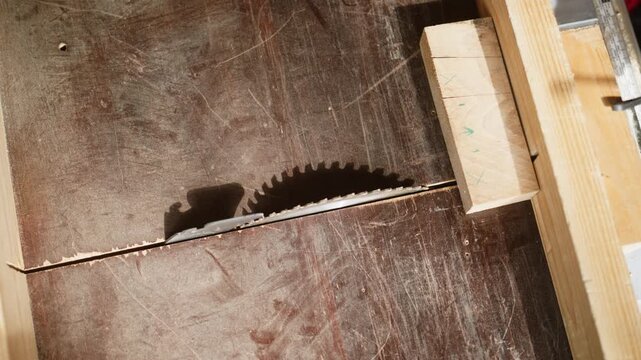 Close-up of a carpenter's hands measuring and marking a wooden block on a workshop table. The scene captures the careful preparation before cutting wood with a circular saw.