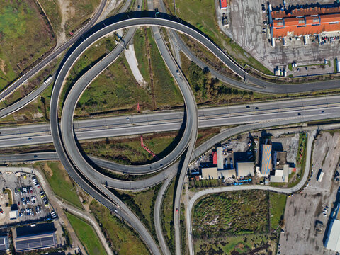 Aerial view of the intricate dance of highways and cloverleaf interchange, a symphony of concrete curves against a backdrop of industrial structures, Kalochori, Thessaloniki, Greece.