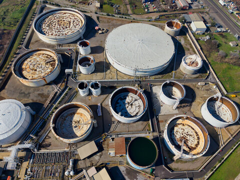 Aerial view of silver tanks gleaming under the sun, contrasting with the dark green liquid within one, surrounded by industrial infrastructure, Kalochori, Thessaloniki, Greece.