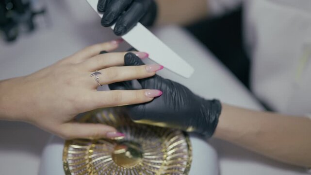 A manicurist meticulously files a client's nails, showcasing a beauty salon service. Professional nail care involves shaping and perfecting hands for a polished look.