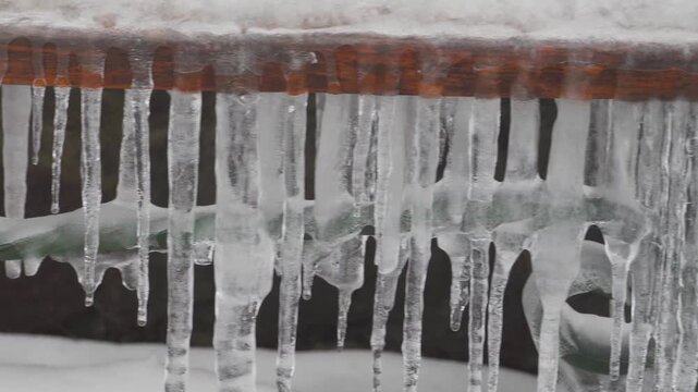 Close-up of frozen icicles hanging from a wooden railing in winter, A row of crystal clear icicles dripping from a wooden edge against a blurred winter background