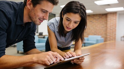 Diverse Young Professionals Collaborating in Modern Office: Focused Man and Woman Using Tablet for Creative Project in Bright Industrial Shared Workspace