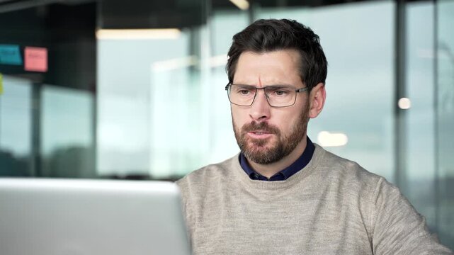 Close-up of frustrated businessman working on laptop in office. Stressed professional reacts with anger and disappointment after computer problem, showing irritation and emotional tension during work.
