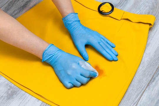 A woman removes a stain from her skirt. A woman's hand holds a stain remover to remove a dirty spot from a skirt. A greasy stain on a yellow skirt. 