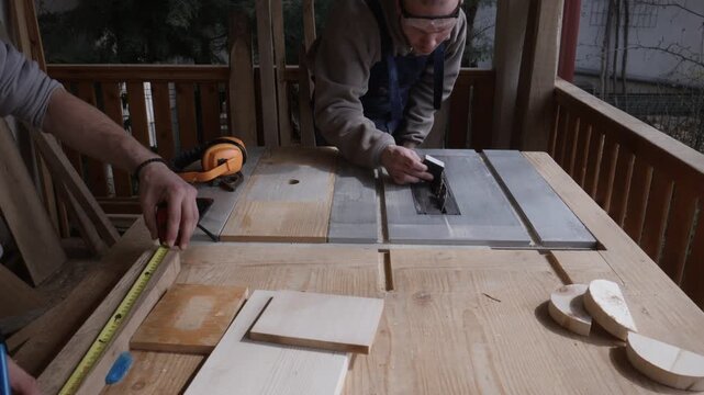 Two men are carefully measuring a piece of wood and setting up a table saw. They are engaged in a precise woodworking project using essential tools and safety gear.
