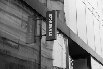 Naklejka premium black and white view of building exterior and projecting sign of Starbucks Coffee Company, a coffee shop chain, located here at 221 Queen St W, Smart House Condo, Toronto