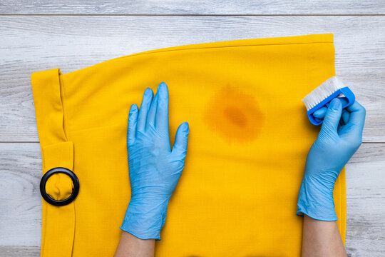 A woman removes a stain from her skirt. A woman's hand holds a stain remover to remove a dirty spot from a skirt. Everyday life concept: a dirty spot that needs to be washed and cleaned. A greasy stai