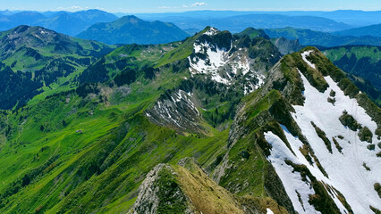 Aerial Drone View of Alpine Ridge with Snow Patches Overlooking Lush Green Valleys and Mountain...