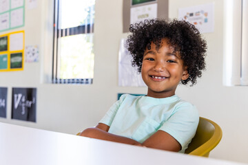 Fototapeta premium African American school-aged boy smiling while sitting in yellow chair at white desk in class