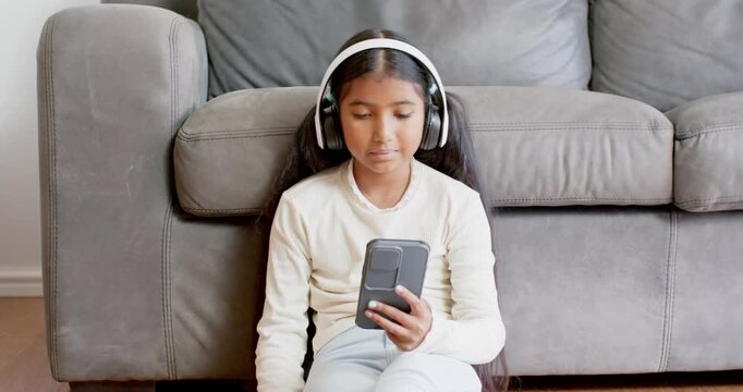 Asian girl wearing headphones at home holding phone while smiling and waving during call
