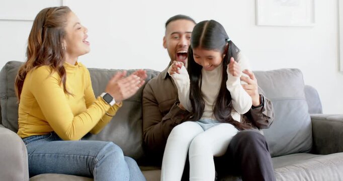 Diverse parents starting tickling daughter on gray couch in living room encouraging joyful laughter