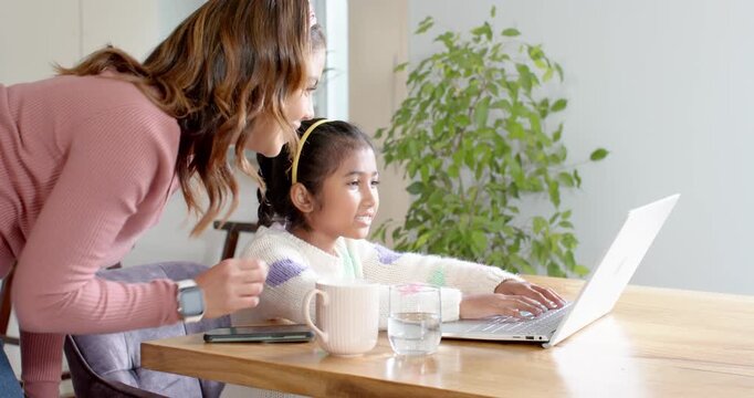 Mother and daughter noticing typing errors at kitchen table, pointing at laptop guiding typing