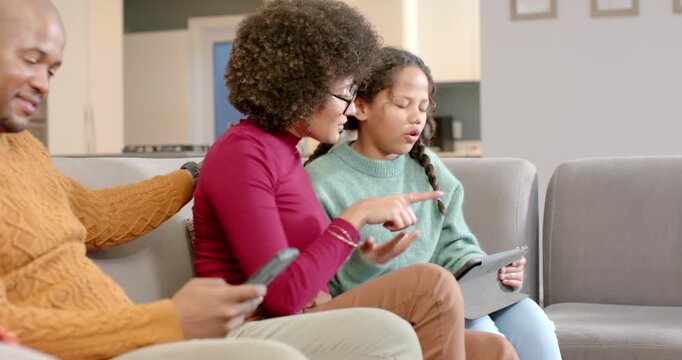 Diverse family on sofa guiding child to navigate tablet after tapping and celebrating high-five