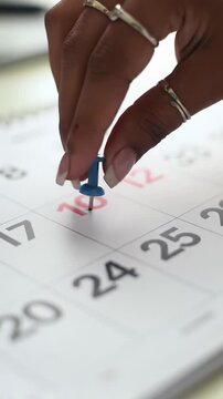 Close-up flat lay video of diverse hands marking dates on a white desk calendar with red & blue pushpins against blurred office. Strategic planning and goal achievement