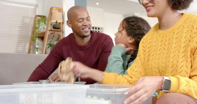 Diverse family teaching recycling, sorting into plastic, paper and glass bins at home living area