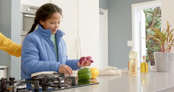 Entering home kitchen with bag African American mother and daughter slicing peppers for dinner prep