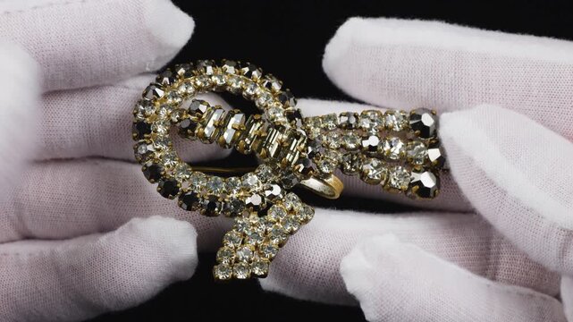 A vintage bow-shaped brooch featuring sparkling white and smoky brown glass crystals. The elegant accessory shines brilliantly as it is presented against a dark background.
