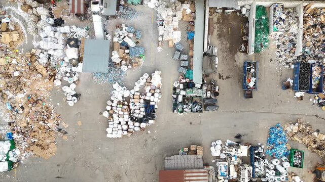 Aerial view of waste sorting and recycling process showing piles of garbage, containers, and vehicles in a waste management facility, highlighting the organization of recyclable materials