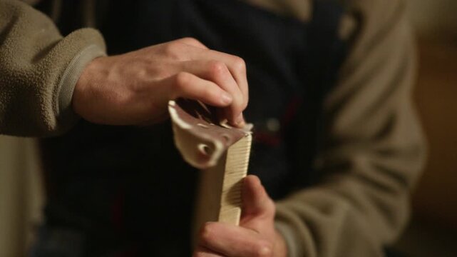 A craftsman meticulously sands a wooden plank by hand, ensuring a smooth surface for his project. Close-up on a person's hands carefully using sandpaper on a piece of wood.