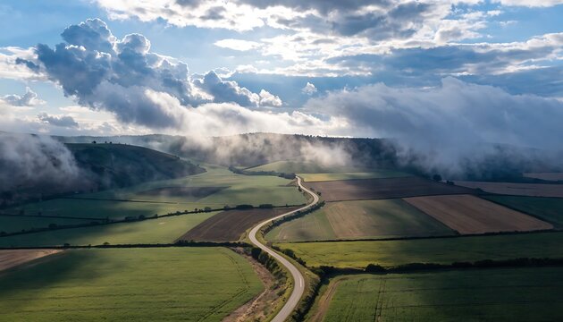 Green landscape with road and foggy clouds rolling over hills high resolution photo