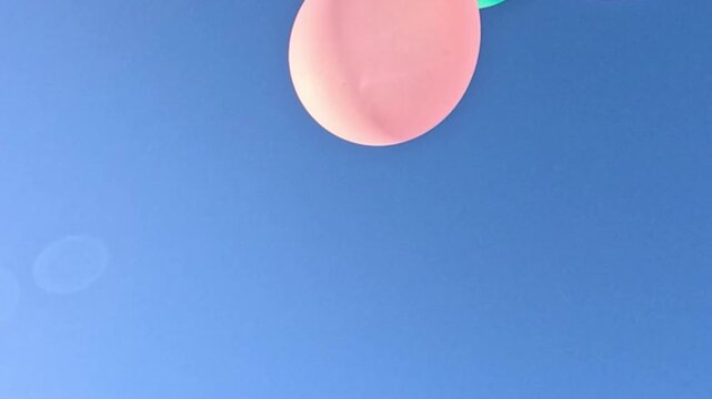 Cluster of pastel balloons drifts upward against a clear blue sky, sways gently in sunlight, then gradually exits the frame, creating a festive birthday, party, and celebration background.