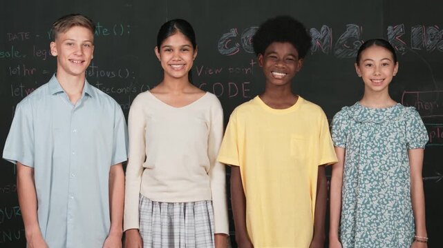 Group of smart multicultural teenager looking at camera at blackboard. Happy diverse children standing in STEM technology class with engineering code, prompt or planning program idea. Edification