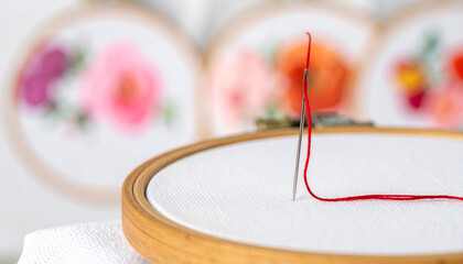 Close up of silver needle pulling bright crimson thread through white fabric in embroidery